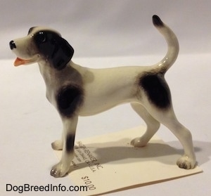The left side of a white with black dog figurine. The tail of the figurine is arched in the air.