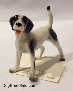 The front left side of a figurine of a white with black dog. The figurine has its mouth open and it looks like it is smiling.