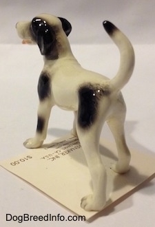 The back left side of a figurine of a white with black. The figurine has long legs.