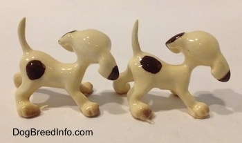 The right side of a two white with brown Hound puppy figurines. The figurines have there long tails arched in the air.