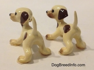The back left side of two two Hound puppy figurines with brown spots toward there back sides.