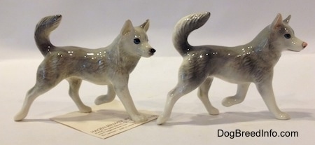 The right side of two grey and white Husky figurines. Both figurines have a paww in the air.