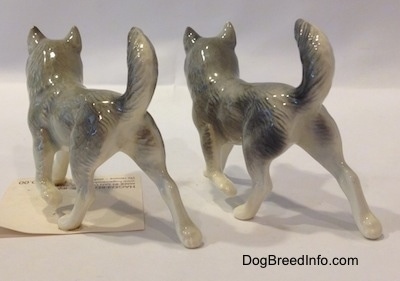 The back left side of two figurines that are Huskys with a paw in the air.