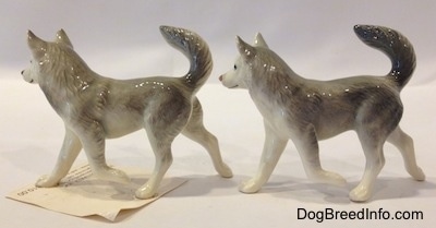 The left side of two grey and white Husky figurines with a paw in the air. Both figurines have there tails arched in the air and their ears are standing up in the air.