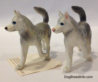 The front left side of two figurines of Huskys with a paw in the air. The figurines have black circles for eyes.
