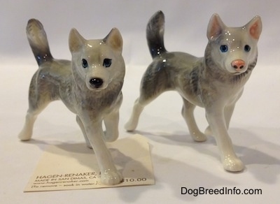 The front right side of two grey with white Figurines and they both have a paw in the air. The figurines are looking forward. One has a grey inner ear and the other has pink inner ears.