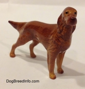 The front left side of a figurine of a brown Irish Setter. The figurine has a tail that sticks out and it is level with its body.