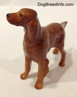 The front left side of a brown Irish Setter figurine that has its head turned to the left. It has hairy ears and its ears are hard to differentiate from its body.