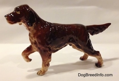 The left side of a brown with tan ceramic Irish Setter that is pointing. The figurine is glossy and its front right paw is in the air.