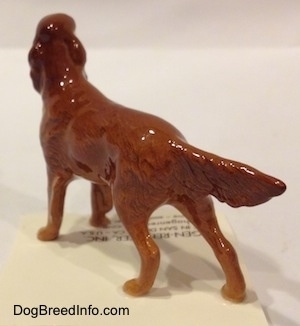 The back left side of a brown Irish Setter figurine. The figurine has a glossy body.