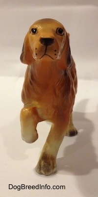 The front of a brown with tan Irish Setter ceramic figurine. The figurine is pointing and it has black spots for whiskers.