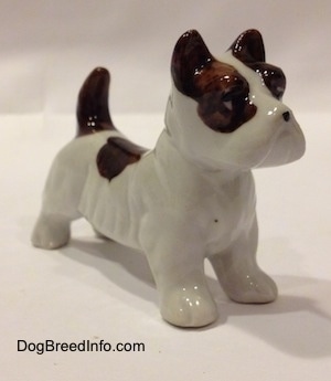 The front left side of a white with brown bone china Jack Russell Terrier dog figurine. The figurine has a black circle for a nose.