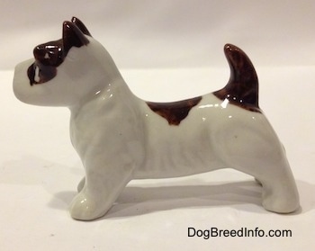 The left side of a white with brown bone china Jack Russell Terrier dog figurine. The figurine has short legs and a short body.