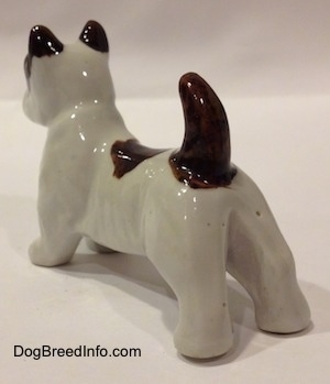 The back left side of a white with brown bone china Jack Russell Terrier dog figurine. The figurine is glossy.