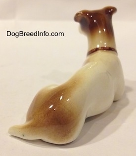The back right side of a white and brown Jack Russell Terrier figurine in a laying down pose. The figurines tail is wrapped around its leg.
