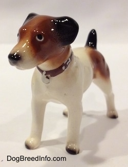 The front left side of a Jack Russell Terrier dog figurine. The figurines tails is in the air