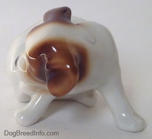 A white with brown Jack Russell Terrier figurine that is scratching its neck.
