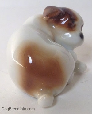 The back side of a white with brown Jack Russell Terrier figurine that is scratching its neck. The figurine has a short tail.
