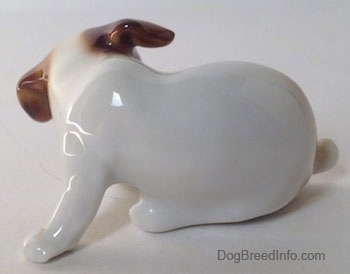 The left side of a Jack Russell Terrier figurine that is scratching its neck. The figurine lacks details in its paws and it has short legs.