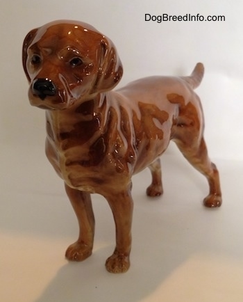 The front left side of a brown Labrador Retriever figurine. The figurine has black circles for eyes and they are detailed.