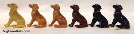 The left side of a line-up of Hagen-Renaker miniature Labrador Retrievers and their different color variations. Each figurine has a different colored collar.
