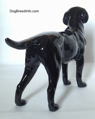 The back right side of a figurine of a black Labrador Retriever figurine. The figurine has its tail up and level with its body.