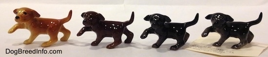 The left side of four Labrador Retriever puppy figurines in different color variations. The figurines have there right paws in the air.