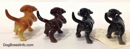 The back of four Labrador Retriever puppy figurines in different color variations.