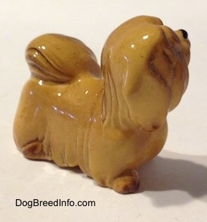 The front right side of a figurine of a tan Lhasa Apso figurine. The figurine is looking up and to the right.