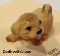 The front left side of a figurine of a Lhasa Apso puppy that is in a walking pose. The tail of the figurine is curled up on its back.