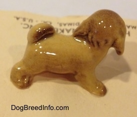 The right side of a brown figurine of a Lhasa Apso puppy. The ears of the figurine are hard to differentiate from the head.