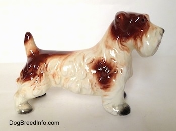 The right side of a white with brown figurine of a Lucas Terrier. The figurine has brown spot on its right side and one at the end of its tail.