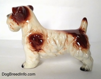 The left side of a white with brown Lucas Terrier figurine. The figurine has black nails at the tips of its short paws.