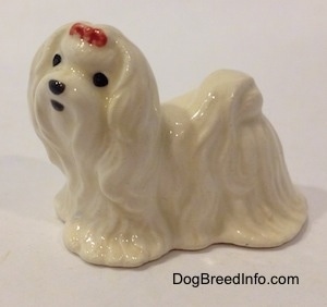 The left side of a white Maltese figurine with a red ribbon in its hair.