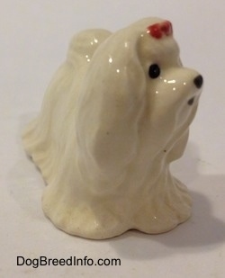 A white Maltese figurine with a red ribbon in its hair. The figurine has short legs.