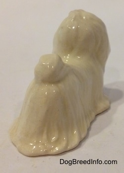 The back right side of a figurine of a white Maltese figurine with a red ribbon in its hair. It is hard to differentiate the ears of the figurine from the head.
