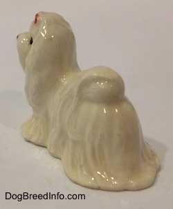 The back left side of a white Maltese figurine with a red ribbon in its hair. The figurine has great hair details.