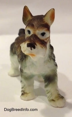 A bone china figurine of a grey and white Miniature Schnauzer. The figurine has black circles for eyes and its mouth is painted open.