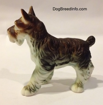 The left side of a figurine of a grey and white bone china Miniature Schnauzer. The figurine has fine hair details along its body and legs.
