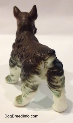 The back left side of a bone china grey and white figurine of a Miniature Schnauzer. The figurine has its small tail arched in the air.