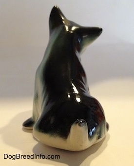 The back of a ceramic black, gray and white figurine of a sitting miniature Schnauzer. The figurine has a short tail above its back.