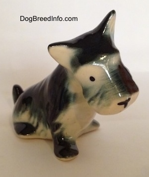 A black, gray and white ceramic Miniature Schnauzer figurine that is in a sitting position. The figurine has black circles for eyes.