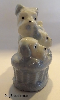 The left side of a bone china figurine that is of a Miniature Schnauzer next her basket of puppies. The figurines have black circles for eyes.