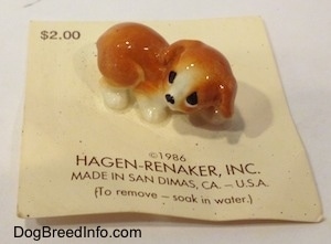 A figurine of an orange and white puppy. The figurines is placed on top of a 'Hagen-Renaker, inc.