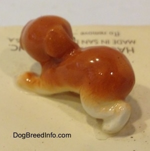 The back left side of an orange and white puppy figurine. The figurine is glossy.