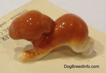 The left side of a figurine of an orange and white puppy figurine. The ears of the figurine are hard to differentiate from the body.