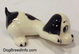 The right side of a white with black puppy figurine that is in a lying pose. The figurine has its right paw in the air.