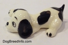The left side of a white with black puppy figurine that is in a lying pose. The figurine has a short black tail.