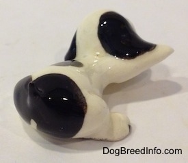 The back right side of a figurine of a white with black puppy in a lying pose. The figurines ear and lifted paw are attached.