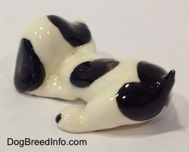 The back left side of a white with black puppy figurine in a lying pose.